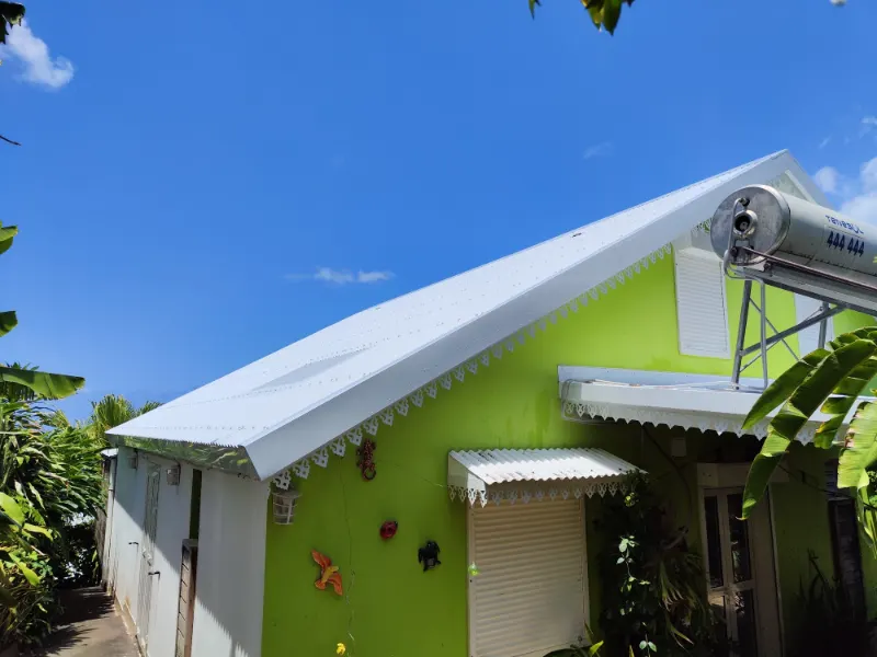 Toiture blanche bordée de lambrequins sur une case aux murs verts.